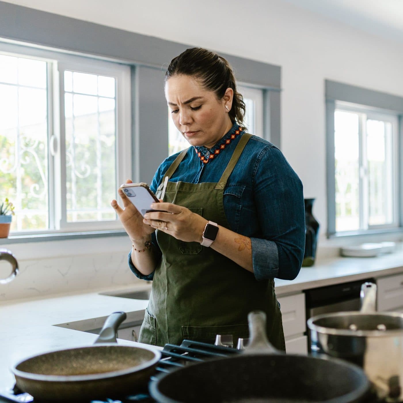 Una mujer mira su celular con cara de duda frente a la cocina de su casa
