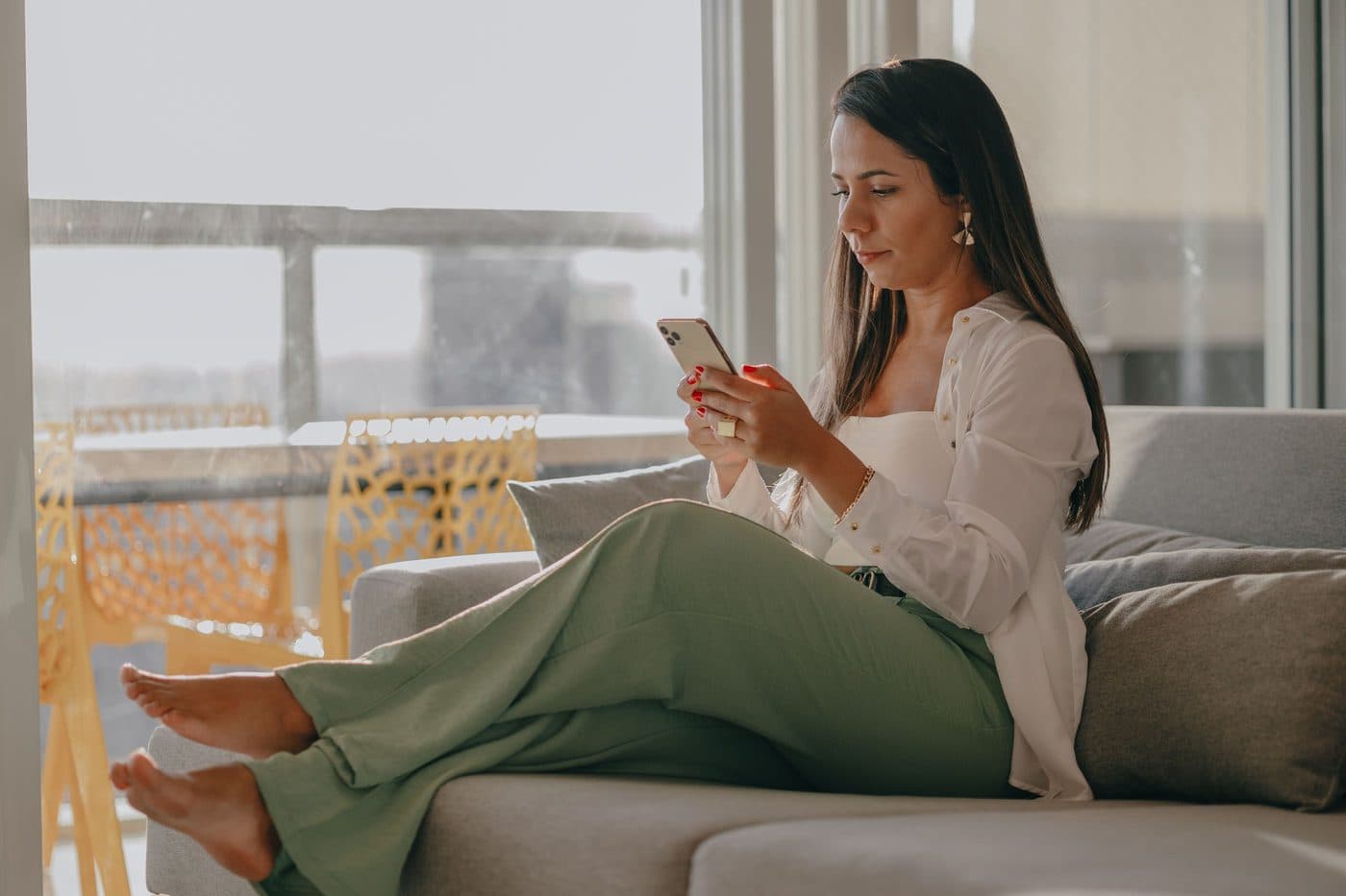 Una mujer revisa su celular sentada en el sillón de su living